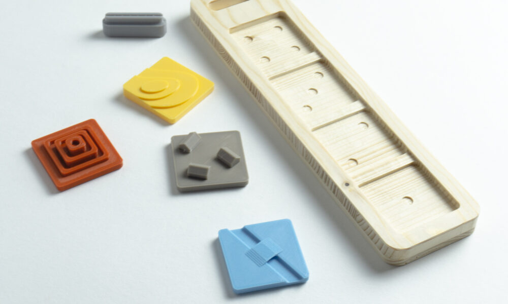 Version démontée d'un outil ludique composé de pièces imprimées en 3D et d'un socle en bois découpé. Les pièces sont interchangeables et permettent aux utilisateurs de tester des configuration différentes.